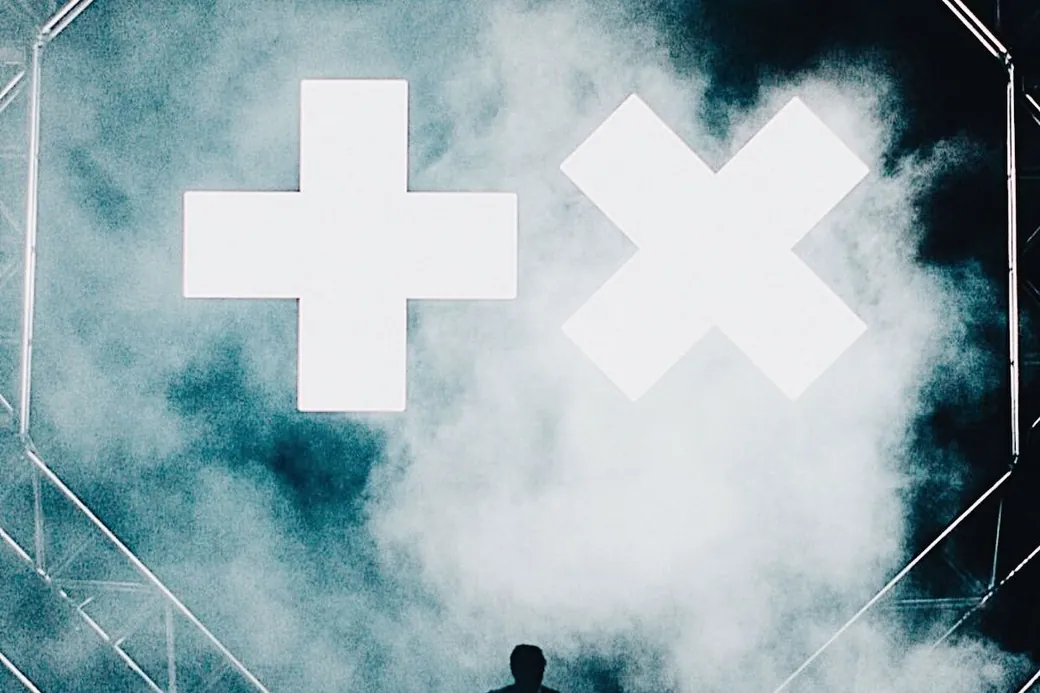 Martin Garrix on stage under the plus and cross logo.